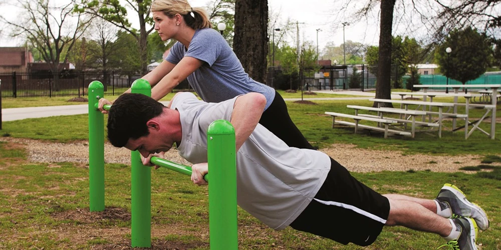 People performing push-ups on outdoor fitness bars for upper body strength training in a park